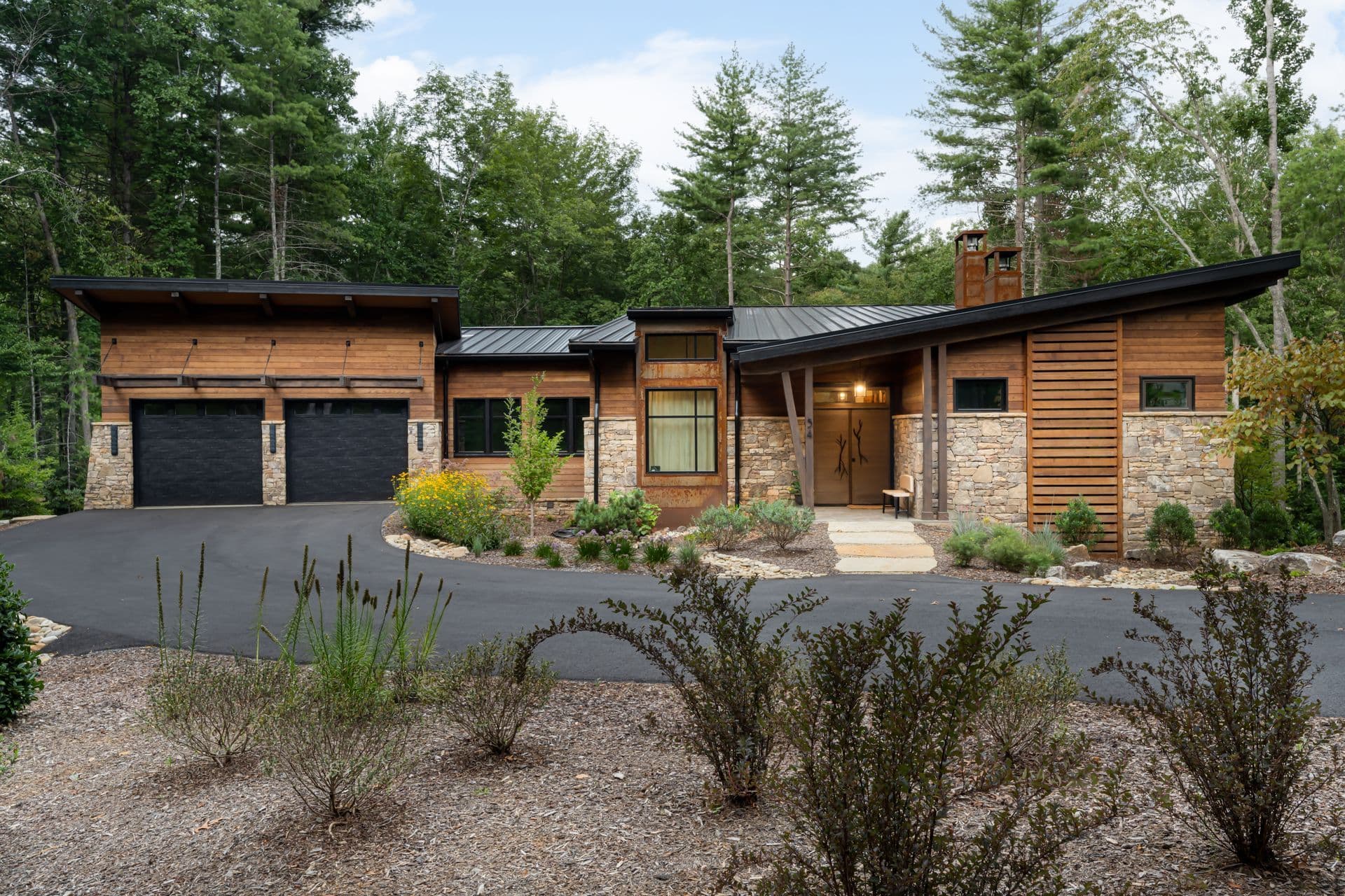 Modern mountain home surrounded by trees, viewed from the driveway