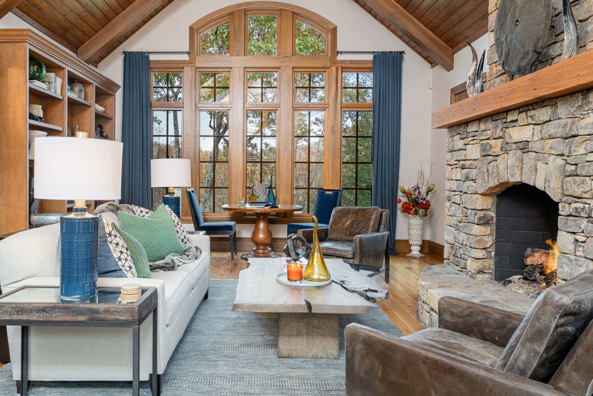 Mountain retreat living room with a stone fireplace, timber ceiling and layered vintage furnishings