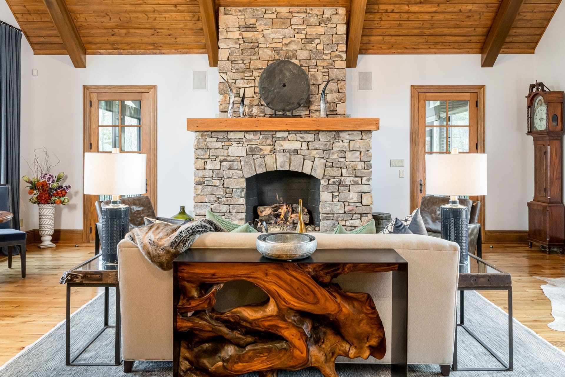 Living room with a stone fireplace, timber ceiling and collected furnishings in a mountain home